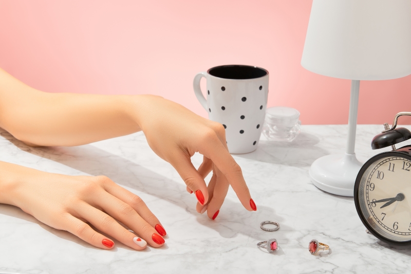 A woman with red nails with rings and a cup of coffee on a table